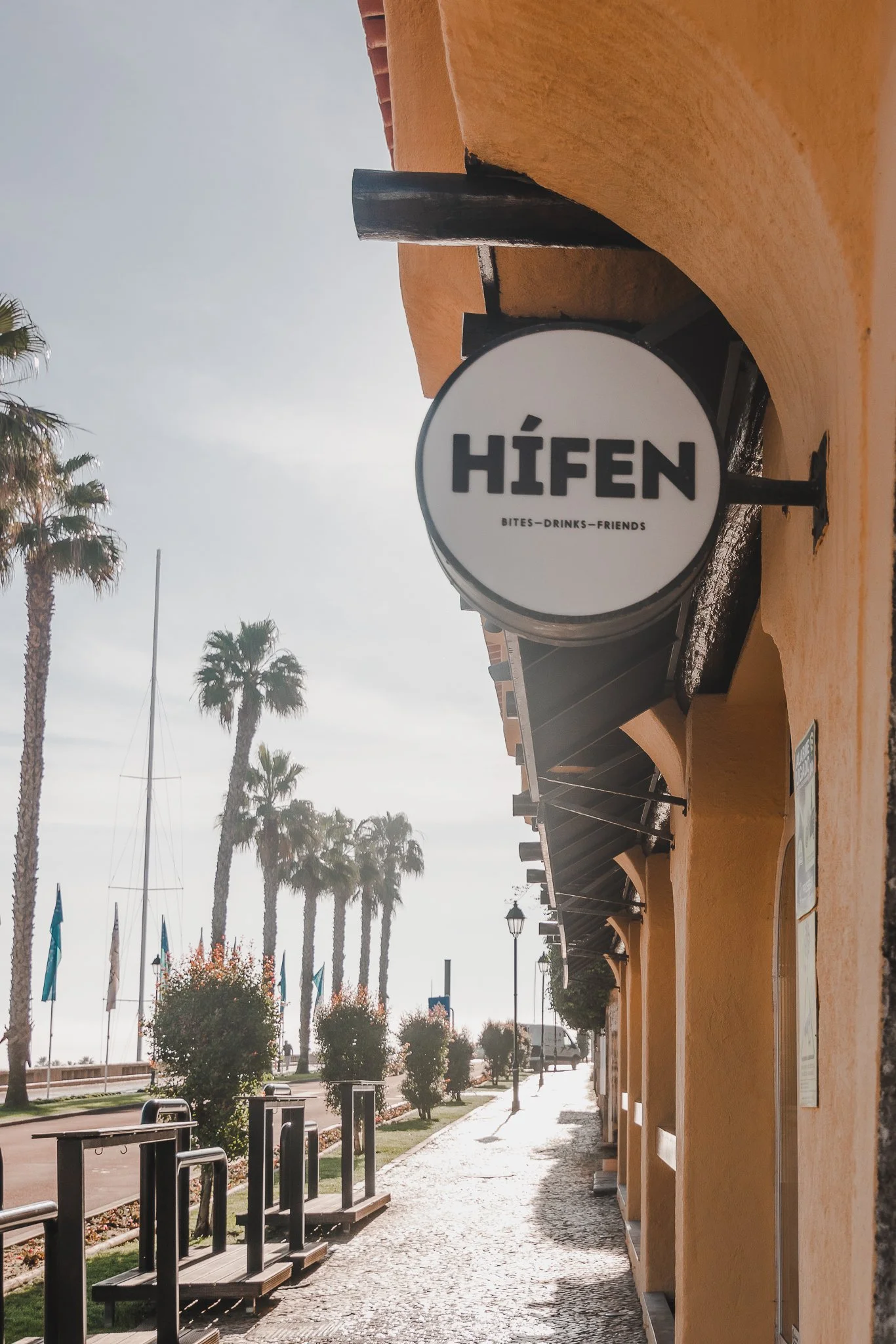 Hífen round sign, street facade and palm-lined pavement